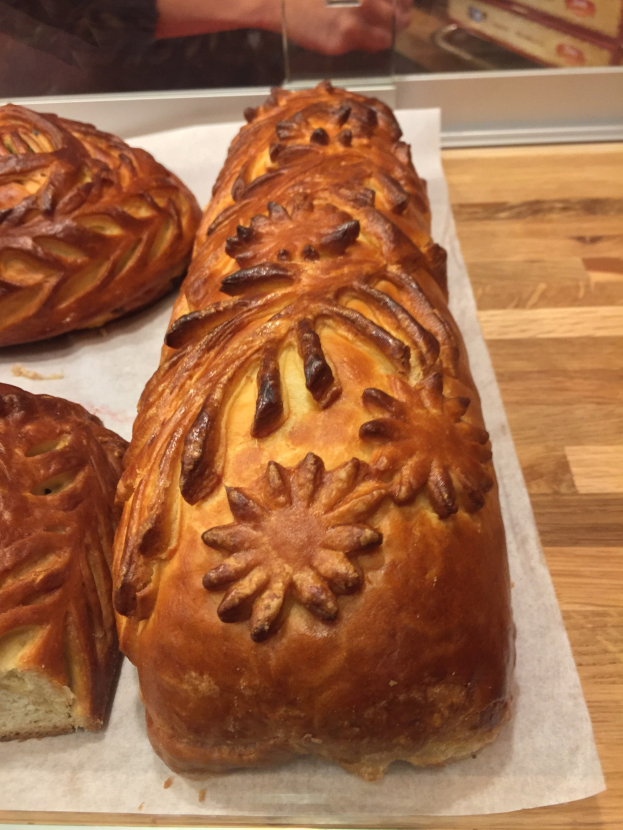 Frisch gebackenes Brot mit goldbrauner Kruste auf einem Holztisch, mit einer Person Hand auf der linken Seite.