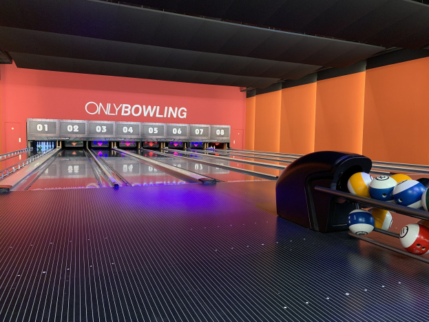 Eine Bowlinganlage mit Bowlingkugeln auf der rechten Seite, Bowlingpins in der Mitte und einer textbedeckten Wand im Hintergrund, mit der Decke oben.