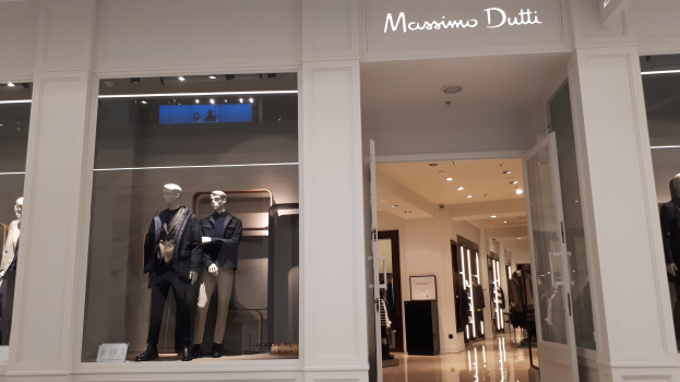 Ein Massimo Dutti Geschäft in Mailand, Italien, mit Schaufensterpuppen in modischen Auslagen, beleuchteter Decke, Texttafeln und sichtbarem Boden.