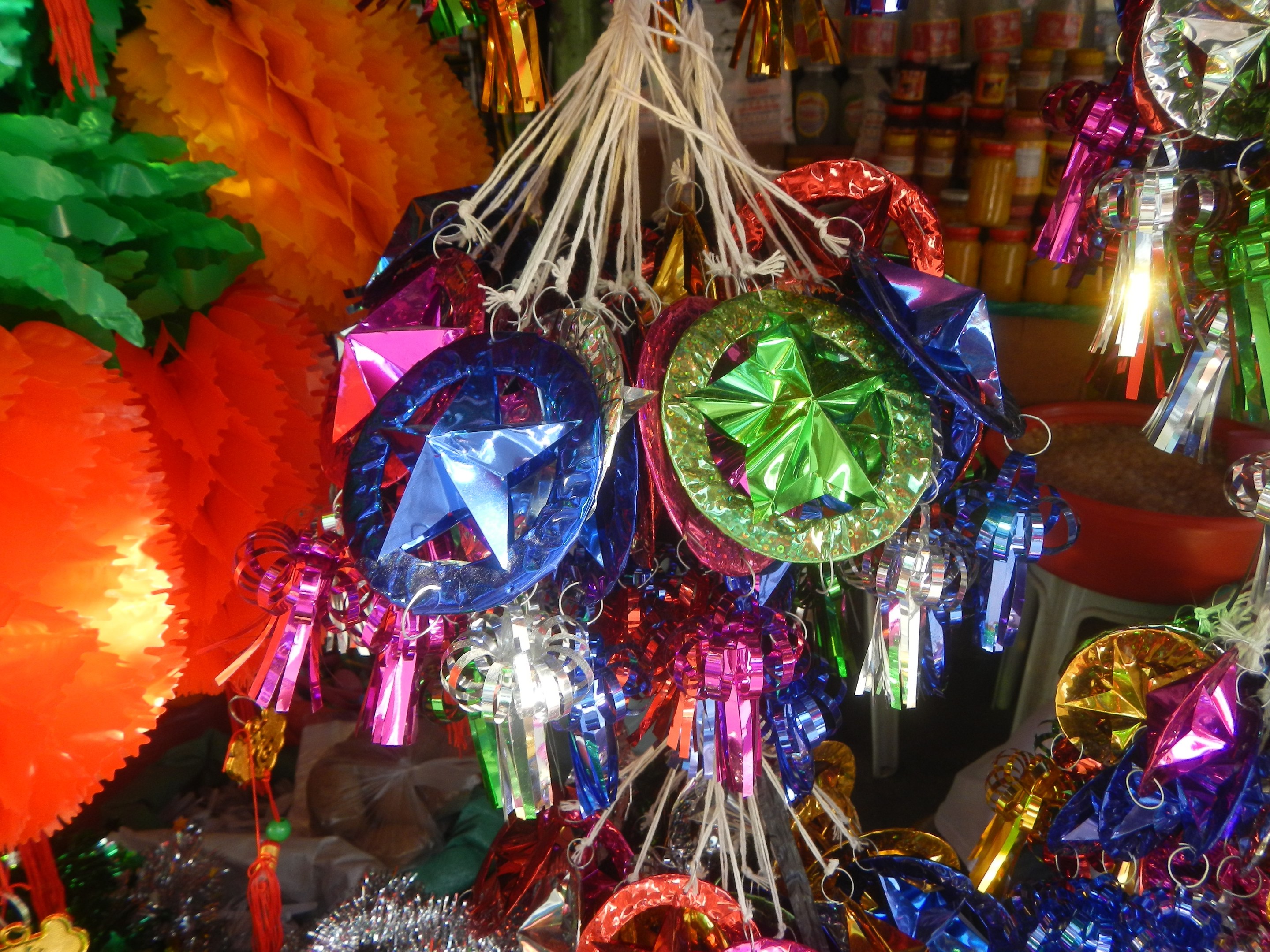 Farbenfrohe Dekorationen wie Papierlaternen und Bänder hängen von der Decke über Regalen voller Flaschen in einer festlichen Atmosphäre.