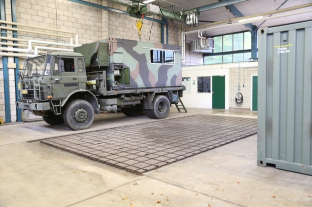 Militaerlastwagen in einem Gebaeude mit einem Container, Wand, Tuere, Rohren, Staebe, Lampen und anderen Gegenstaenden.