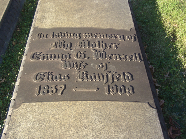 Grabstein mit der Inschrift "Die liebevolle Erinnerung an meine Mutter" in einem grasbewachsenen Friedhof umgeben von trockenen Blättern.