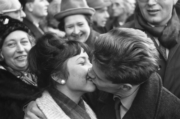 Ein Schwarz-Weiß-Foto eines Mannes und einer Frau, die leidenschaftlich vor einem lachenden Publikum knutschen.