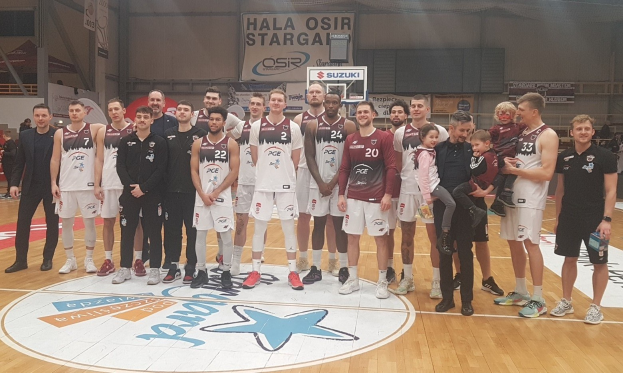 Gruppe von Männern und Kindern auf einem Basketballfeld mit Schildern, auf denen "Hala Osir Starga" steht, im Hintergrund.