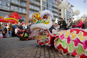 Eine Löwen-Tanzvorstellung während eines chinesischen Neujahrsfestes in Amsterdam, mit einer Zuschauermenge und Gebäuden im Hintergrund.