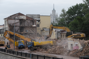 Eine belebte Abrissszene in Kiew, Ukraine, mit Kränen, Fahrzeugen, Menschen, Pfählen, Lichtern, Schildern, Geländern und Bäumen, mit sichtbarem Himmel und einem Wasserzeichen auf dem Bild.