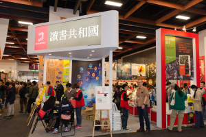 Eine große Gruppe von Menschen an einem Messestand mit Stühlen, Texttafeln, Bannern und Deckenbeleuchtung, die "Book Republic Hong Kong Book Fair" liest.
