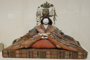 Eine Statue einer Frau in einem Kimono sitzt auf einem Tisch mit einer Wand im Hintergrund.