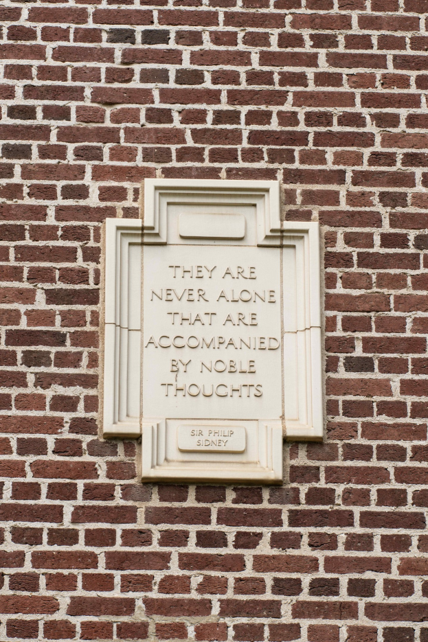 Steintafel an einer Ziegelwand mit der eingravierten Inschrift "Sie sind nie allein, die von edlen Gedanken begleitet sind".