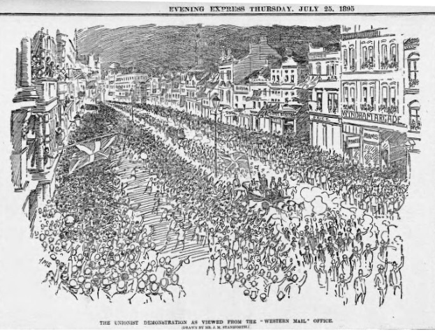 Schwarze und weiße Zeichnung einer Menge, die eine von Gebäuden gesäumte Straße entlanggeht, mit Text oben und unten, der lautet: "Die Unionistendemonstration, wie sie vom Western Mail Office aus zu sehen ist."
