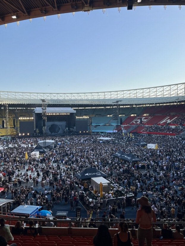 Große Menschenmenge auf Sitzplätzen und Stehplätzen in einem Stadion mit Zelten, Geländern und Beleuchtung während eines Events in der O2 Arena in London.