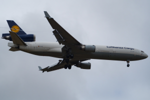 Ein Lufthansa Cargo Boeing 777-300ER-Flugzeug im Flug, mit ausgebreiteten Flügeln und aktivierten Triebwerken, das durch einen Himmel voller weißer, flauschiger Wolken fliegt.