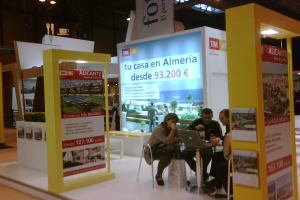 Eine Gruppe von Menschen, die um einen Tisch sitzen und auf einen Laptop schauen und arbeiten, mit mehreren Flyern mit verschiedenen Werbeanzeigen daneben.