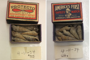 Zwei Streichholzschachteln mit der Aufschrift 'Protecto' und 'Amerikas erste Sicherheitsstreichholzschachtel' auf einem Tisch mit verschiedenen Gegenständen darin und zwei nummerierten Papieren unten.