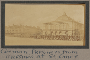 Eine Gruppe deutscher Gefangener aus Messines steht vor einem Gebäude an einem klaren blauen Himmel, mit Text unten im Bild.