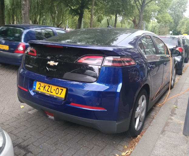 Elektrisches Auto an einer Ladestation auf einer von Bäumen gesäumten Straße unter einem klaren blauen Himmel.