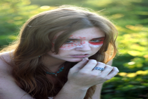 Eine Frau mit Make-up im Gesicht steht vor Grünzeug.