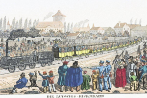 Eine Gruppe von Menschen, die um einen Zug auf einem Gleis stehen, mit einigen im Zug sitzend und anderen außerhalb stehend, in der Nähe von Gebäuden und Bäumen, mit Text unten lesend "Ludwigs-Eisenbahn, der erste Bahnhof in Deutschland"