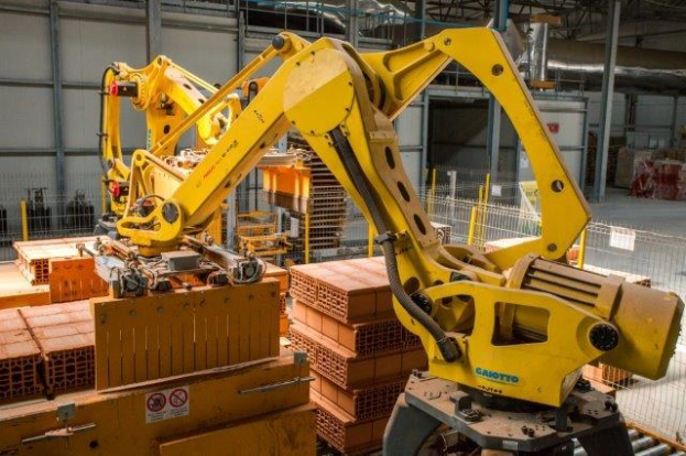 Großes industrielles Lager mit gestapelten Kisten, Kränen, Zäunen, Pfählen und einer fernen Wand in einer automatisierten Fertigungsumgebung.
