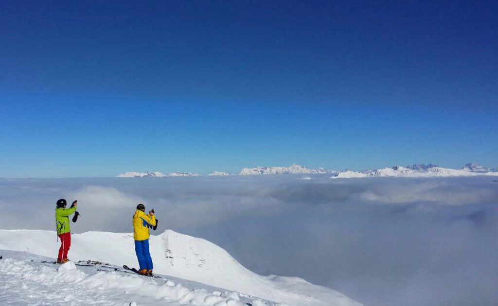Zwei Personen auf Snowboards in einer verschneiten Landschaft, die Gegenstände halten, mit Hügeln und Himmel im Hintergrund.