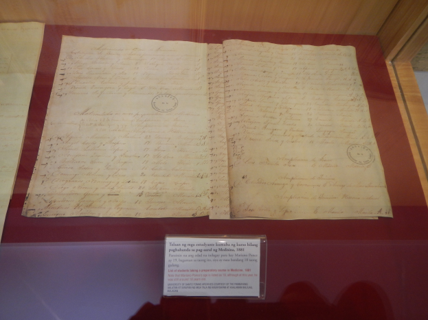 Altes Dokument in einer Glasvitrine mit Text darauf und einer Beschriftung unten, vor einem hölzernen Hintergrund in einem Museum.