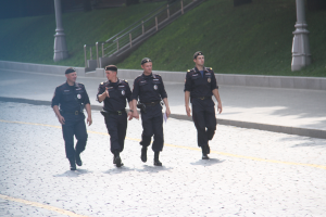 Drei Polizeibeamte in Uniform auf der Straße mit Masten, Geländern, Treppen und Gras im Hintergrund.