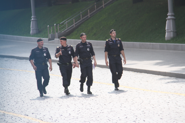 Drei Polizeibeamte in Uniform auf der Straße mit Masten, Geländern, Treppen und Gras im Hintergrund.