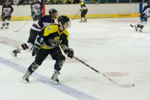 Menschen beim Eishockeyspielen mit Stöcken und Helmen, mit anderen und einer Wand im Hintergrund.