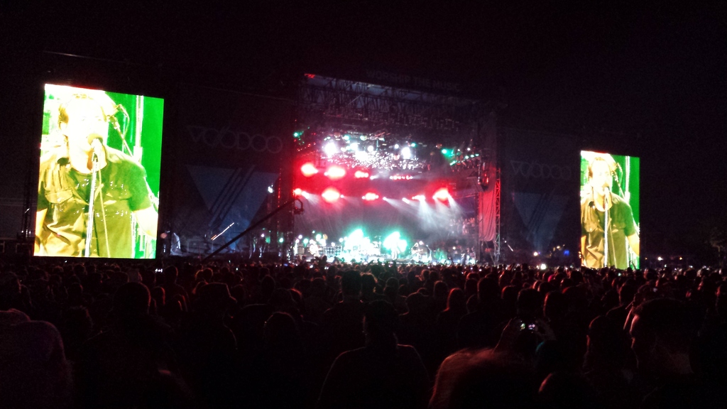 Eine Konzertszene mit einer Menge unten und einem gro├čen Bildschirm links sowie einem kleineren Bildschirm rechts.