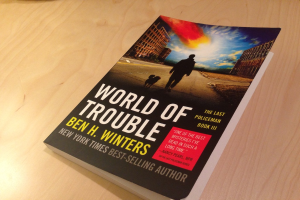 Ein Buch mit dem Titel "World Of Trouble" mit einem Mann und einem Hund auf dem Cover, das auf einem Tisch liegt.