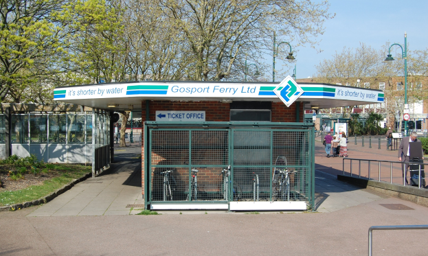 Bus-Haltestellenschild für Gosport Ferry Ltd mit Menschen, Fahrrädern, Bäumen und einem Gebäude unter einem bewölkten Himmel.