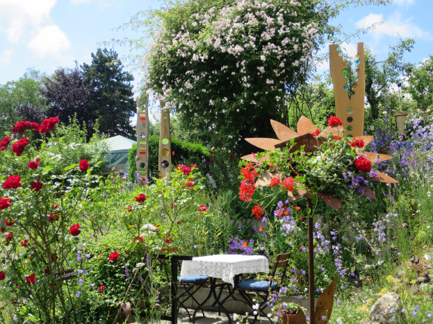 Ein Garten mit bunten Blumen und Pflanzen, mit einem Tisch mit einer Decke und Stühlen, umgeben von Bäumen unter einem bewölkten Himmel auf der Chelsea Flower Show.