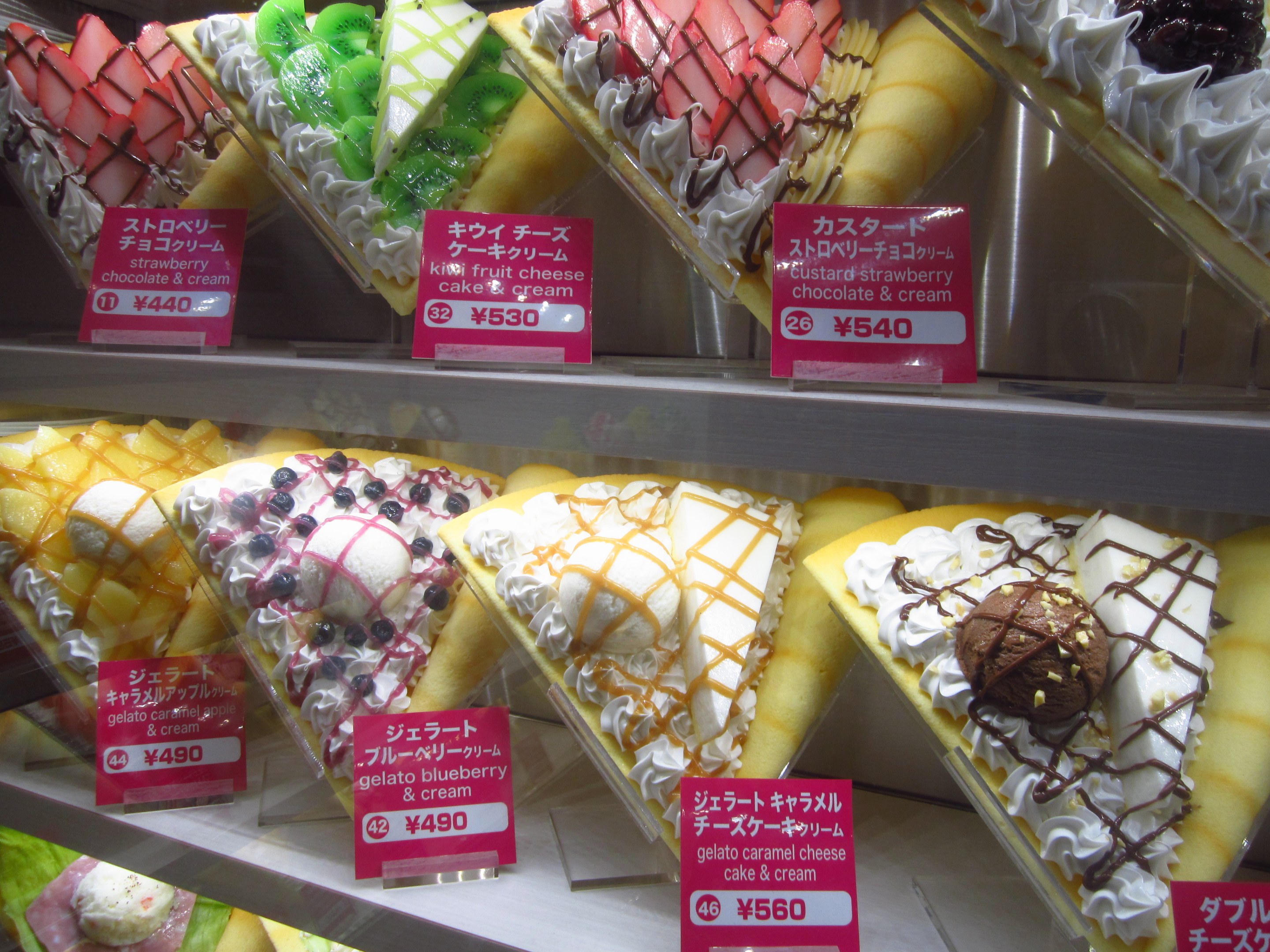 Vitrine mit verschiedenen Sorten Eis, jede mit einem Preisschild, in unterschiedlichen Farben und Formen angeordnet.