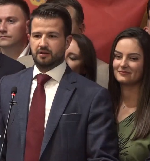 Ein Mann im Anzug und Krawatte steht an einem Rednerpult mit einem Mikrofon und spricht vor einem Publikum mit einem Banner im Hintergrund, wahrscheinlich in Reaktion auf ein Regierungsverbot von Social Media.