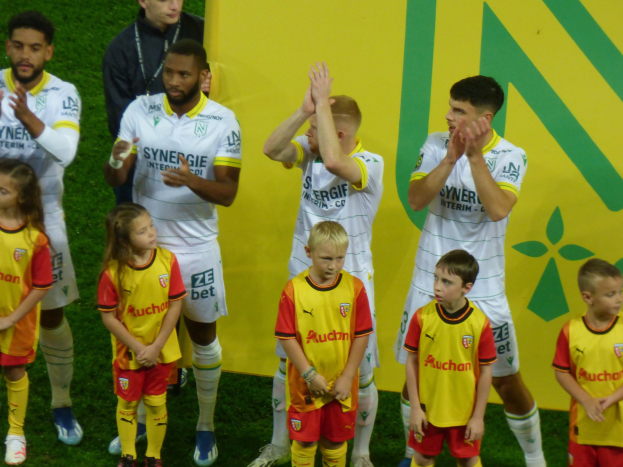 Eine Gruppe junger Förderspieler in Uniformen klatscht auf einem Ligue-1-Feld in celebration, mit einem "Ligue 1"-Schild im Hintergrund.