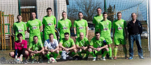 Eine Gruppe von Männern in grünen T-Shirts steht auf einem Fuballfeld, einige hocken, mit einem Ball vor ihnen und einem Torpfosten rechts daneben.