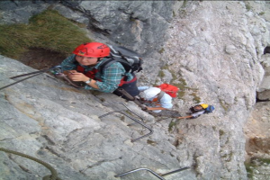 Menschen klettern einen Hügel mit fixen Seilen, tragen Helme und tragen Taschen.