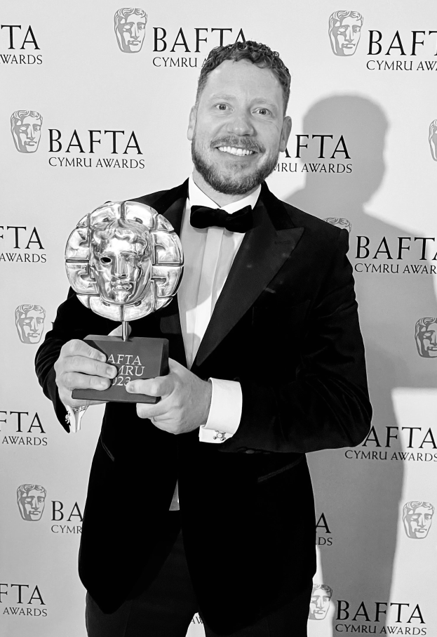 Ein Mann im Smoking, der eine BAFTA-Trophäe hält und lächelt, mit "BAFTA Awards 2018" im Hintergrund.