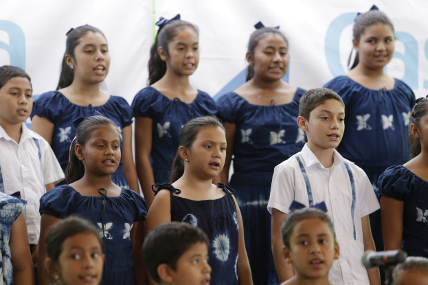 Gruppe von Kindern vor einem Mikrofon stehend und singend mit einem Schulchor-Banner im Hintergrund.