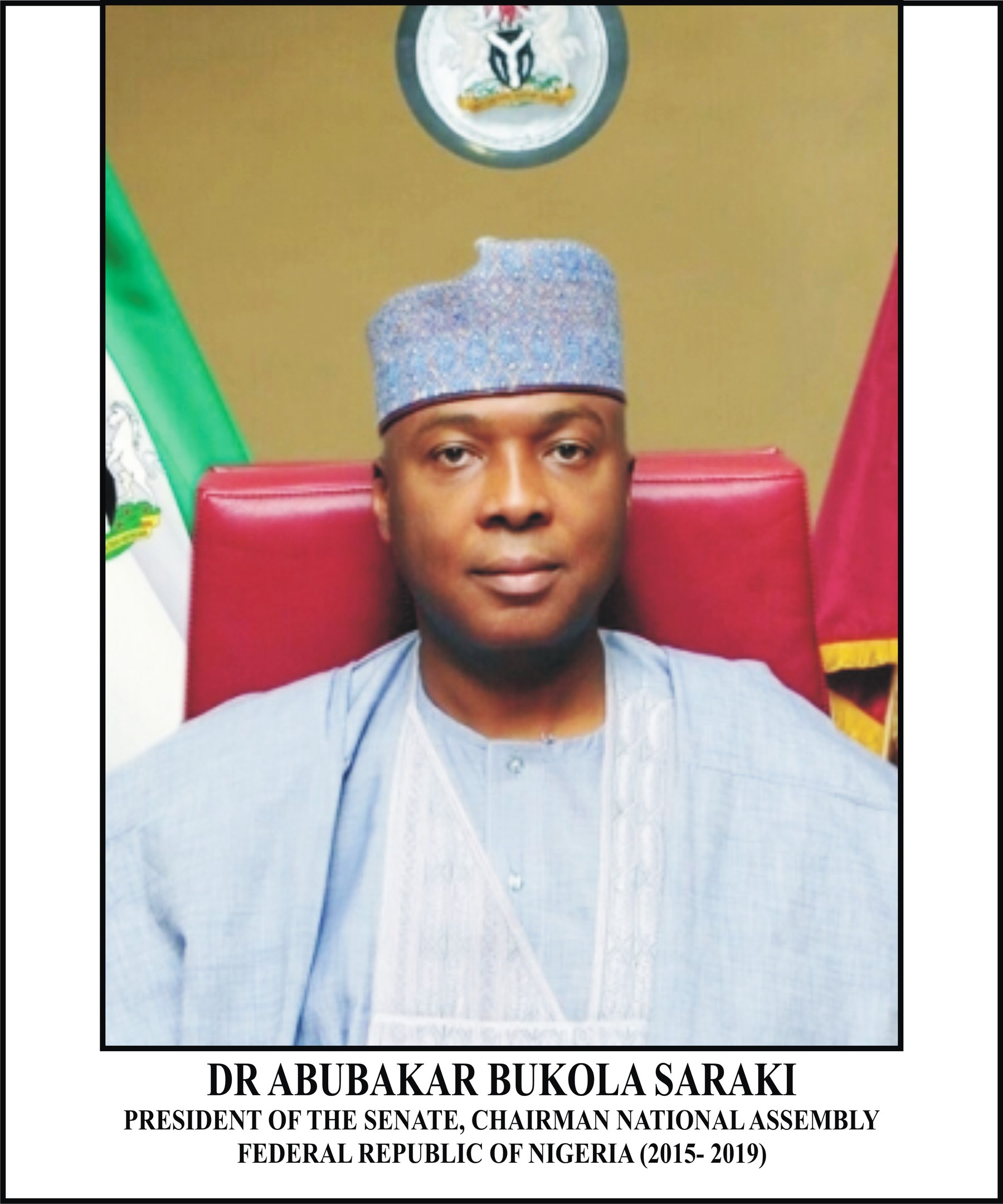 Dr. Abubakar Bukola Saraki, Präsident des Senats und Vorsitzender der Nationalversammlung, sitzt in einem blauen Gewand und Hut, mit zwei Flaggen und einer logogeschmückten Wand im Hintergrund; ein Rahmen mit Inschrift darunter