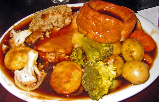 Weißer Teller mit Yorkshire-Pudding, Karotten, Kartoffeln und Zwiebeln auf einem Tisch mit Gläsern und Papiertüchern.