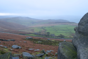Eine malerische Aussicht mit großen Felsen und Steinen im Vordergrund und Feldern und Bergen im Hintergrund.