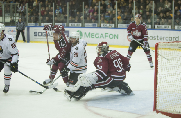 Gruppe von Menschen, die Hockey auf einem Eisstadion mit Tor auf der rechten Seite spielen, tragen Helme und halten Stöcke, Zuschauer auf Tribüne mit Schildern im Hintergrund.