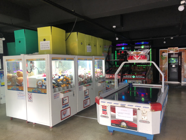 Ein Raum voller verschiedener Arcade-Spiele, mit einem Spielautomaten auf der rechten Seite und sichtbarem Boden sowie Deckenlampen darüber.