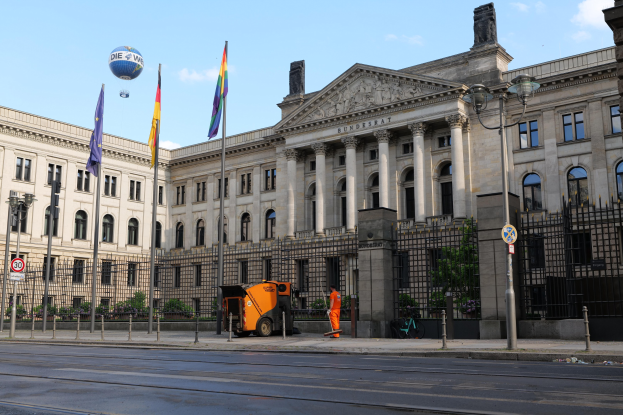 Großes modernes Gebäude mit vielen Fenstern, als Bundestag in Berlin identifiziert, umgeben von Straßeninfrastruktur, Füügängern und Bäumen unter einem bewölktem Himmel.