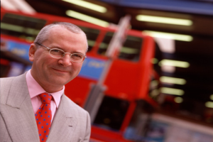 Ein Mann, der strahlt, mit elektrischen Lichtern, Werbung an einem Pfahl und einem Kraftfahrzeug im Hintergrund.