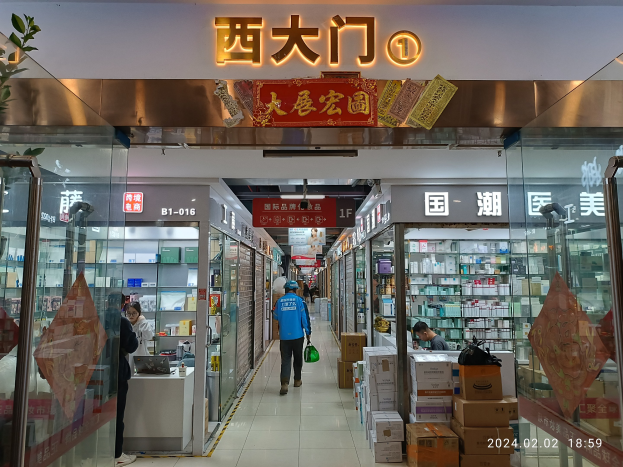 Innenseite einer chinesischen Apotheke mit Glaswänden, Regalen voller Artikel, verstreuten Kartons, einer Pflanze links und einem Namensschild oben, das auf eine chinesische Drogerie hinweist.
