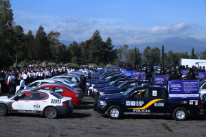 Eine große Anzahl von Polizeiwagen auf einem Parkplatz mit Menschen in der Nähe, Schilder mit Text und ein Hintergrund aus Bäumen, Hügeln und einer bewölkten Himmel.