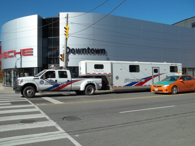Polizeilaster vor einem Gebäude mit Text geparkt, mit einer Ampel und Leitungen im Vordergrund, Bäumen und einem klaren blauen Himmel im Hintergrund.